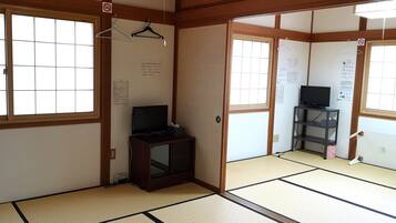 A traditional Japanese room with tatami flooring, a television on a cabinet, and a sliding door.