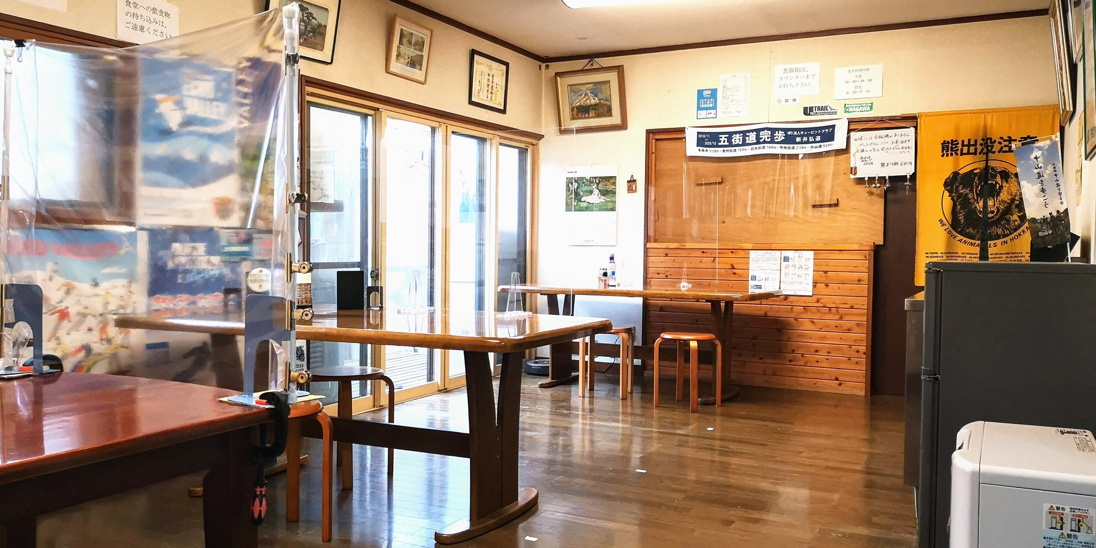 Interior de restaurante con mesas y sillas de madera, una barra y varios carteles y avisos en las paredes.