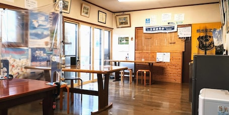 A restaurant interior with wooden tables and chairs, a counter, and various signs and notices on the walls.