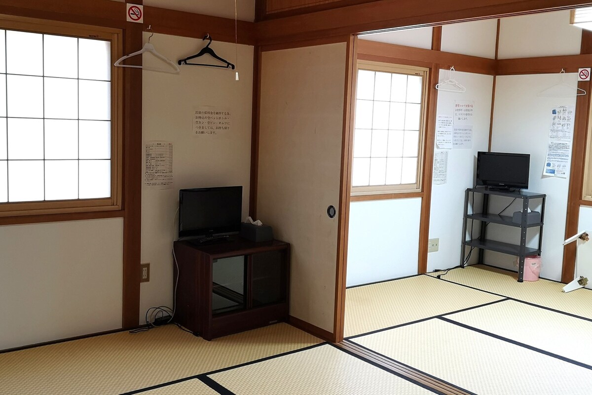 A traditional Japanese room with tatami flooring, a television on a cabinet, and a sliding door.