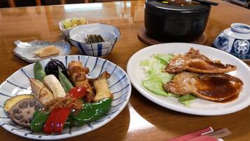 A table with two plates of food, a bowl of pickled vegetables, and a teapot.