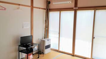 A room with tatami flooring, a television on a black stand, an air conditioning unit, and sliding shoji doors.