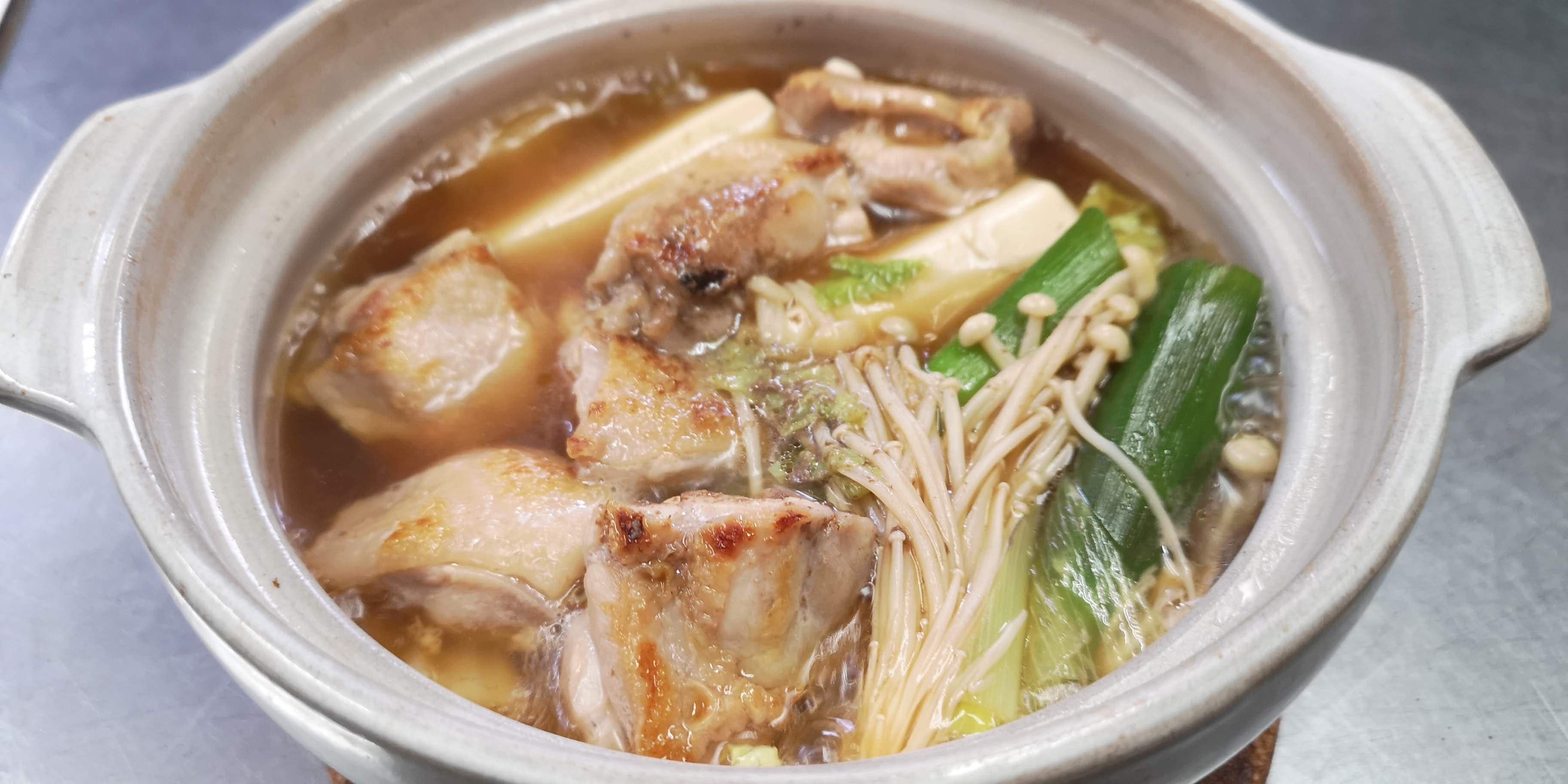 A ceramic pot containing a hot soup with various ingredients.