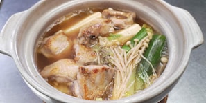 Een keramieken pot met daarin een warme soep en diverse ingrediënten.