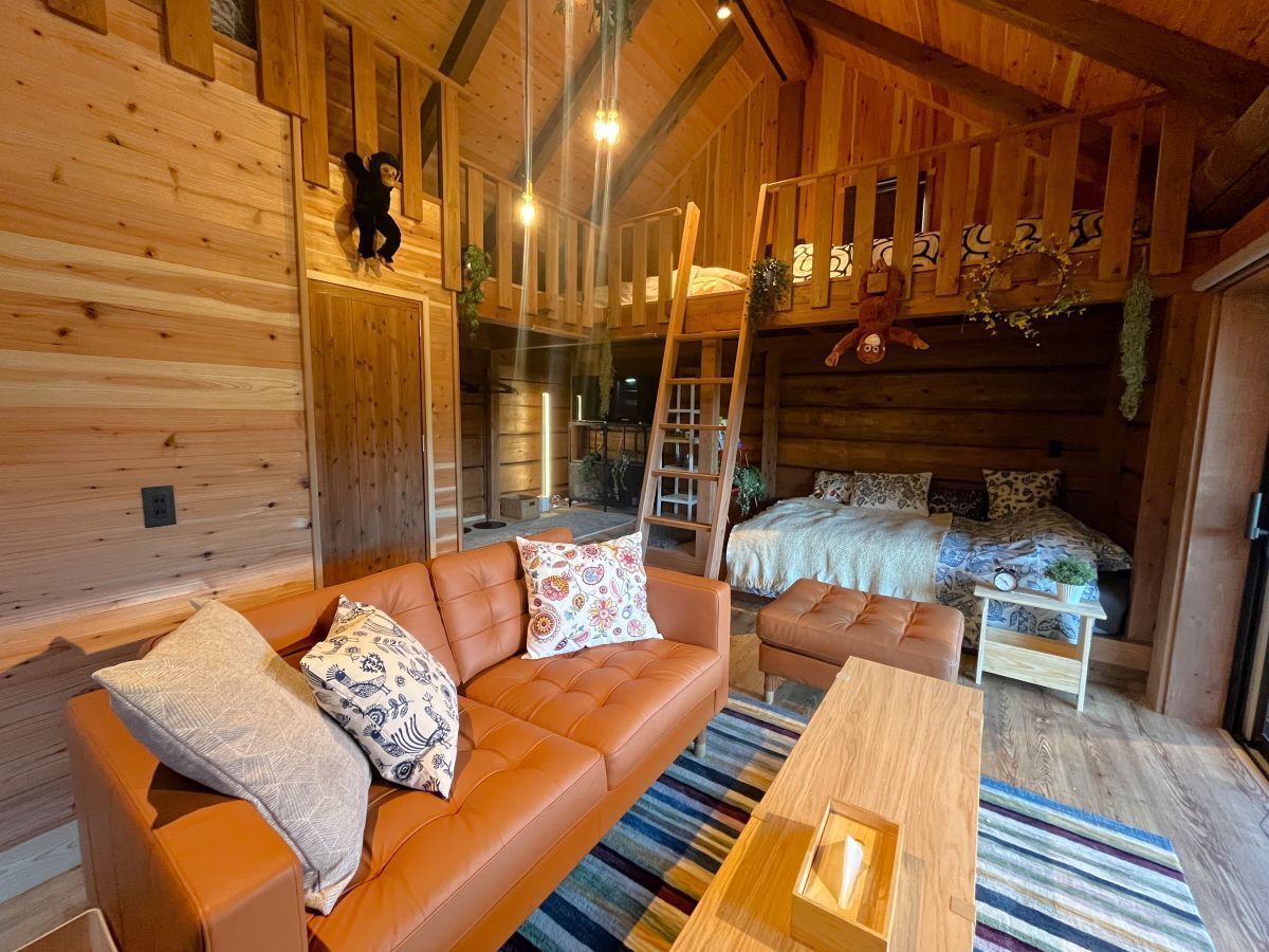 Interior acogedor de una cabaña con paredes de madera, un sofá, una cama y una escalera.
