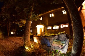 Un edifici de nit amb finestres il·luminades, envoltat d'arbres i un rètol amb mapa i text.