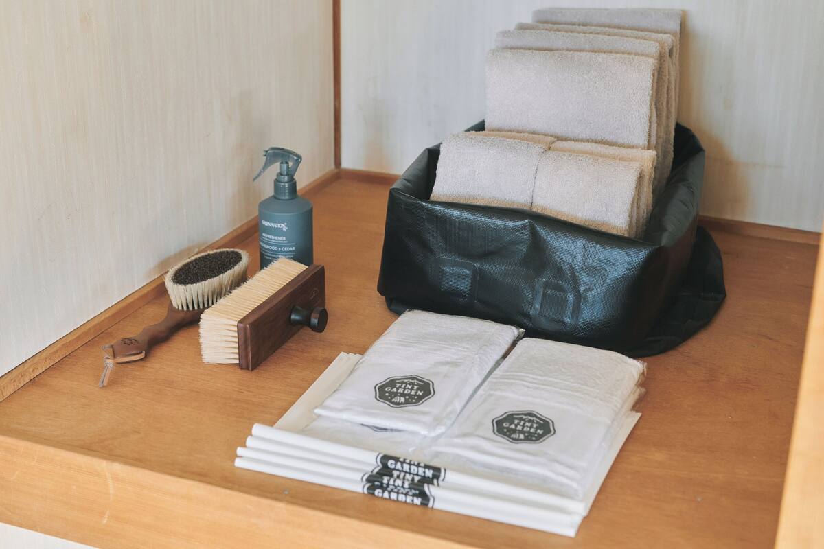 A wooden tray with a black bag, a bottle, a brush, and folded towels.