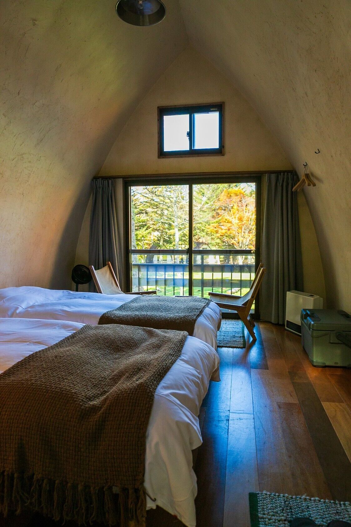 Un dormitorio con dos camas, una ventana con cortinas, una silla, un calentador y una maleta.