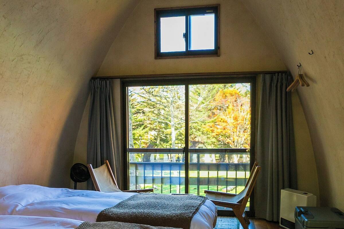 A bedroom with two beds, a window, a chair, and a radiator.