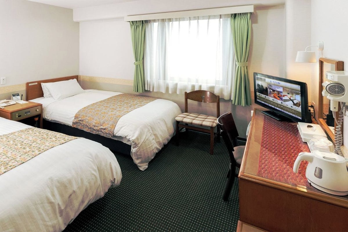 Habitación de hotel con dos camas, un escritorio con televisor, una silla y una cafetera.