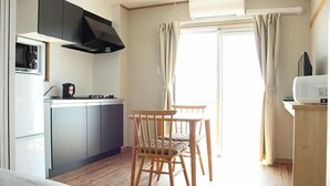 Una cucina compatta con forno a microonde, fornello e mobili, una sedia di legno e una finestra con tende.