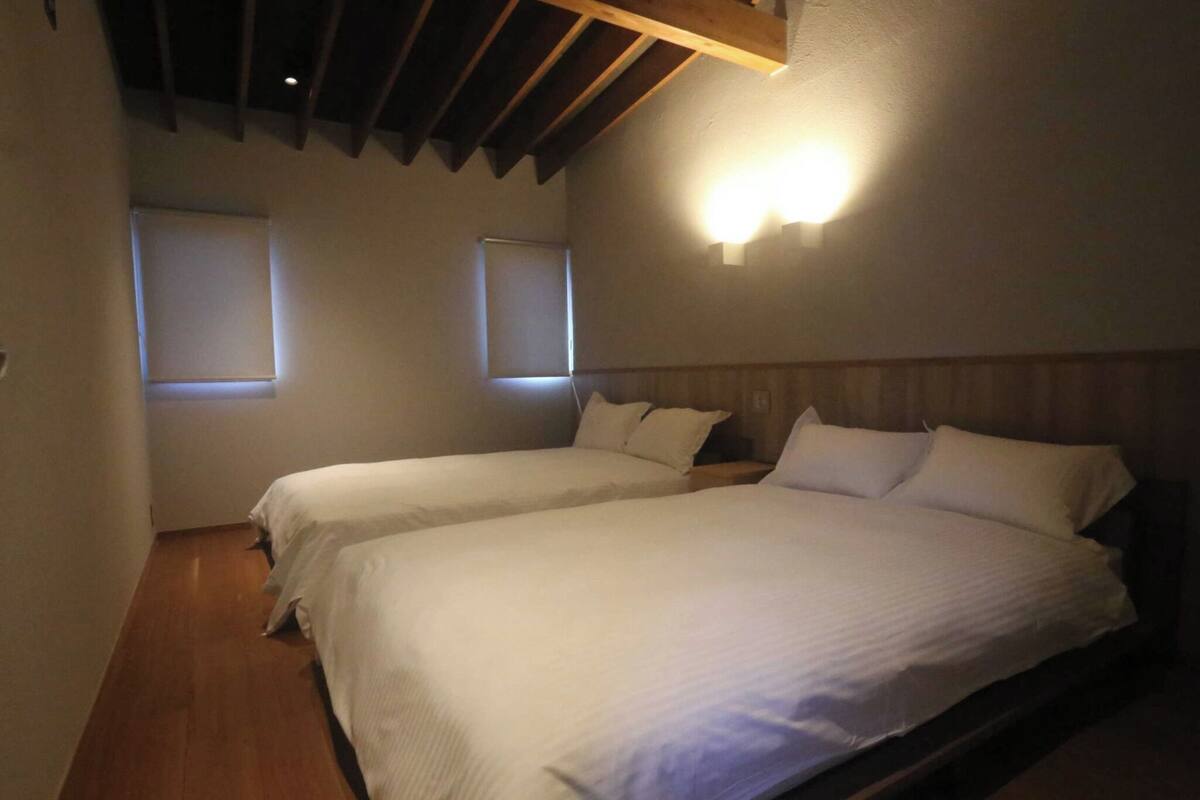 A room with two beds, wooden flooring, and a sloped ceiling with exposed beams.