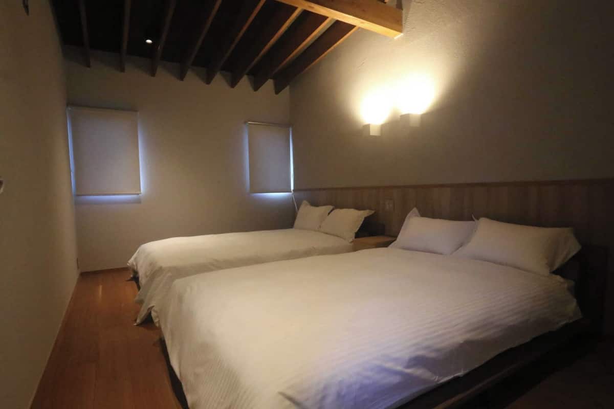 A room with two beds, wooden flooring, and a sloped ceiling with exposed beams.