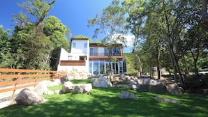 A modern two-story house with a large glass facade, surrounded by a well-maintained lawn and large rocks. - Okutass Resort Villa Terra (Awaji)