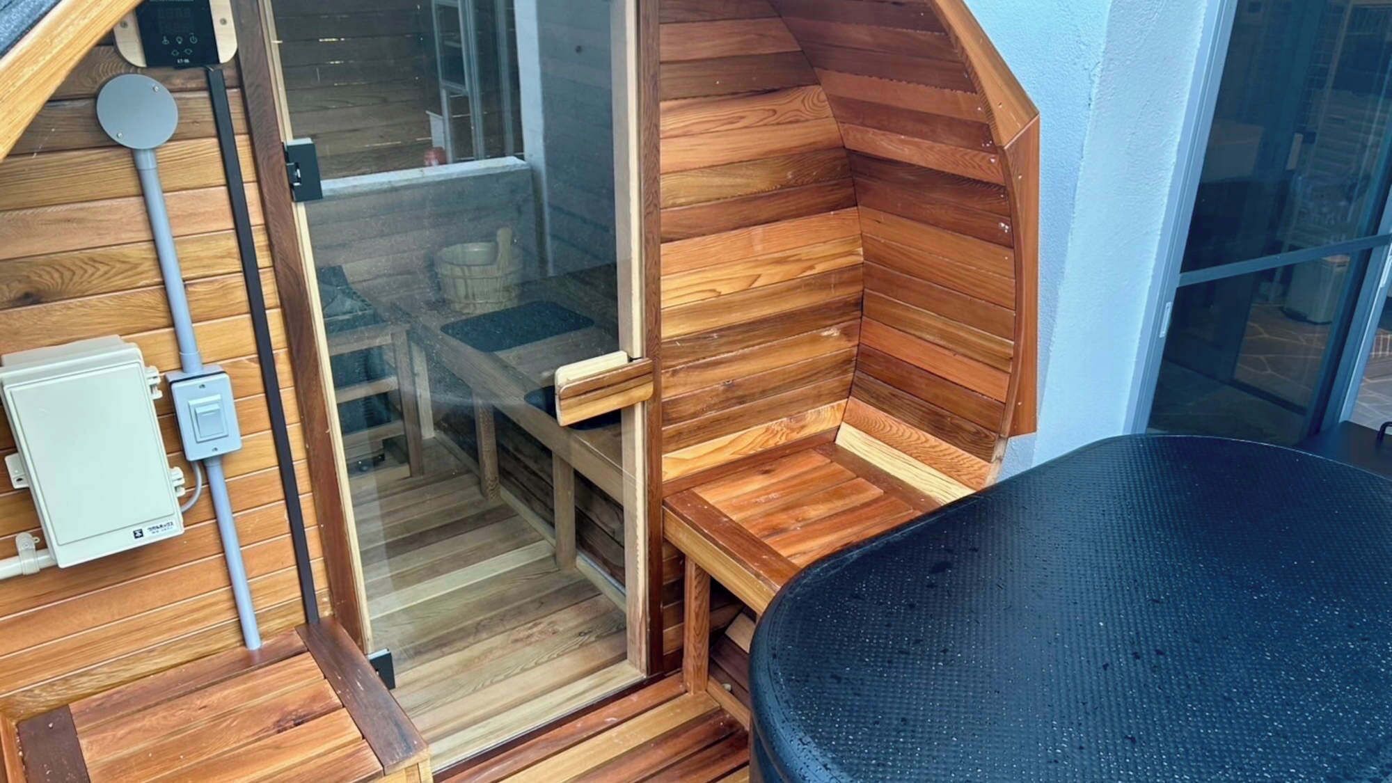Een kleine, knusse kamer met houten wanden en een bankje. Er is een raam en een deur, en een stoel is te zien.