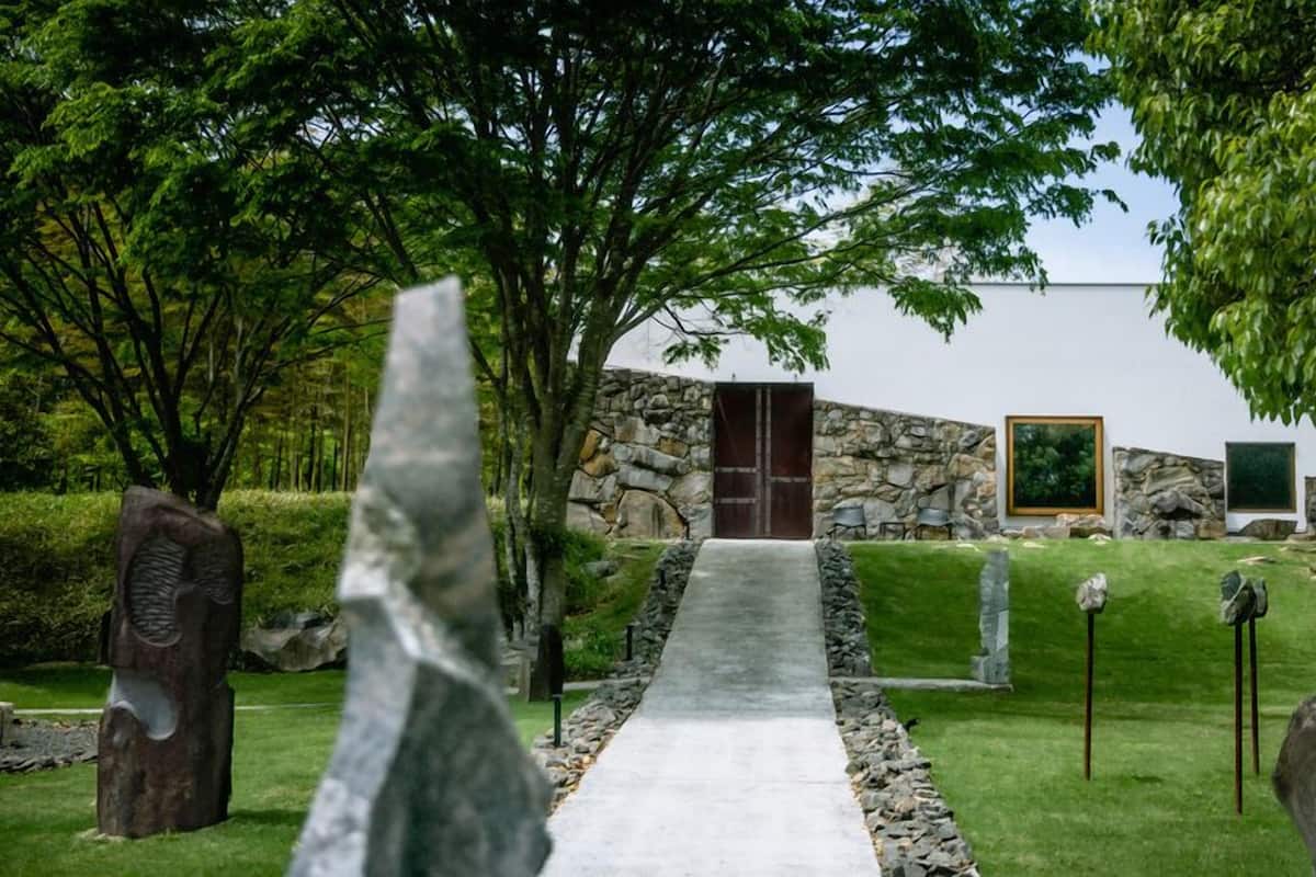 A pathway leading to a stone building with a wooden door, surrounded by stone sculptures and greenery.