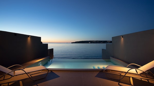 A rooftop infinity pool with two lounge chairs, a clear view of the sea, and a sunset in the background. - Feliz Villa Suite Kourijima View (Nago)