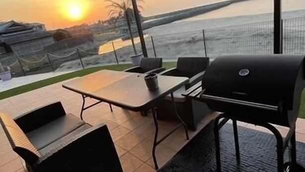 Une terrasse extérieure équipée d’un barbecue, de sièges et offrant une vue sur le coucher de soleil sur l’eau.