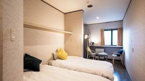 Una habitación de hotel compacta con dos camas, un escritorio pequeño y una silla.