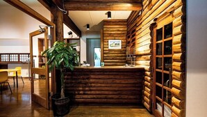 Un área de recepción con paredes de troncos de madera, un mostrador de recepción, una planta en maceta y un comedor con sillas amarillas.