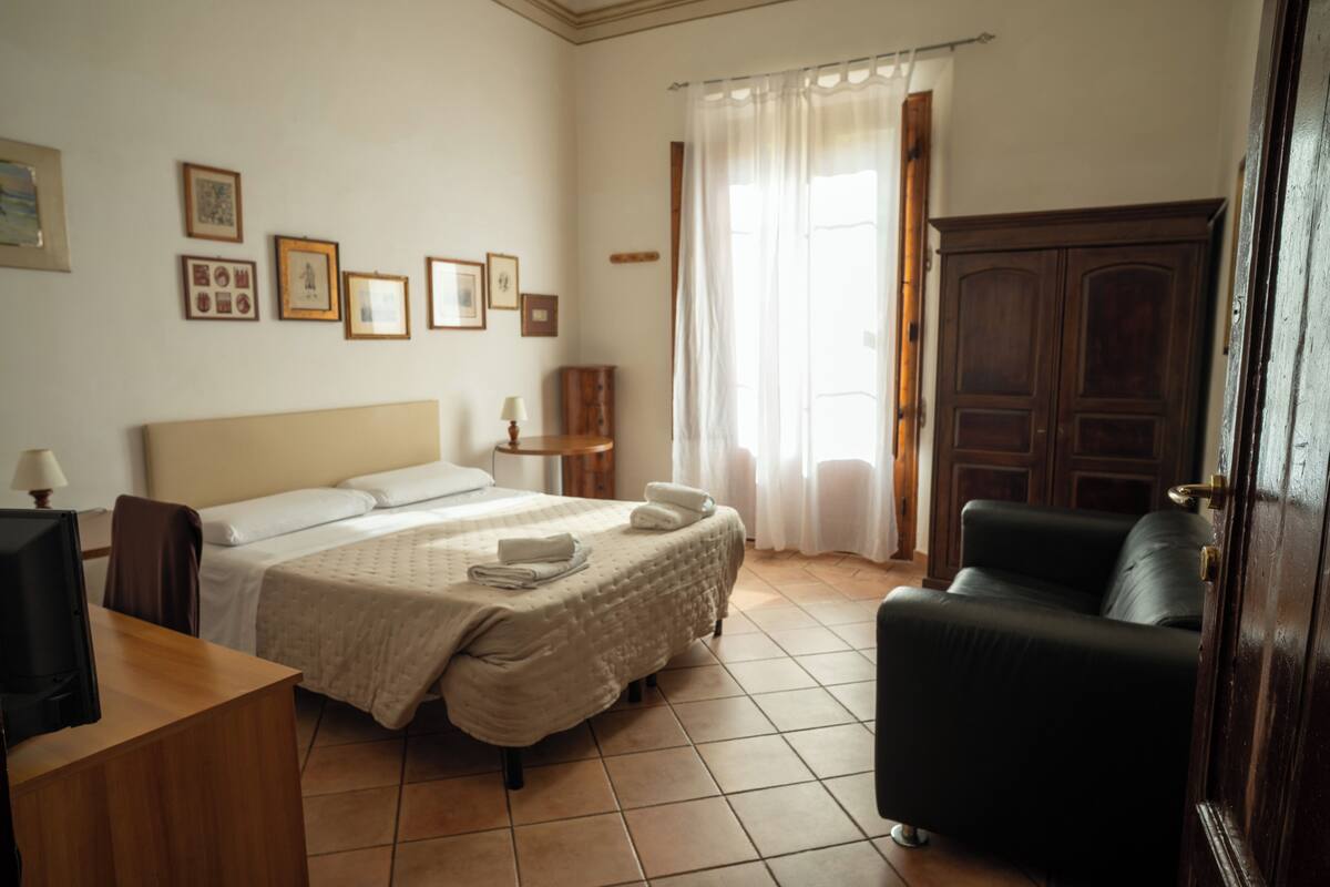 A hotel room with a bed, a desk, a chair, a wardrobe, and a window with curtains.