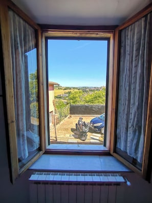 A room with a large window, a piano, and a view of a green landscape. - casa di alfredo (Siena)
