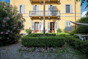 A building with a yellow facade, multiple windows with shutters, a balcony, and a garden area with a table and chairs. - casa di alfredo (Siena)