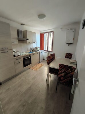 Een moderne keuken met een eethoek, inclusief een tafel, stoelen, een magnetron en een raam met gordijnen.