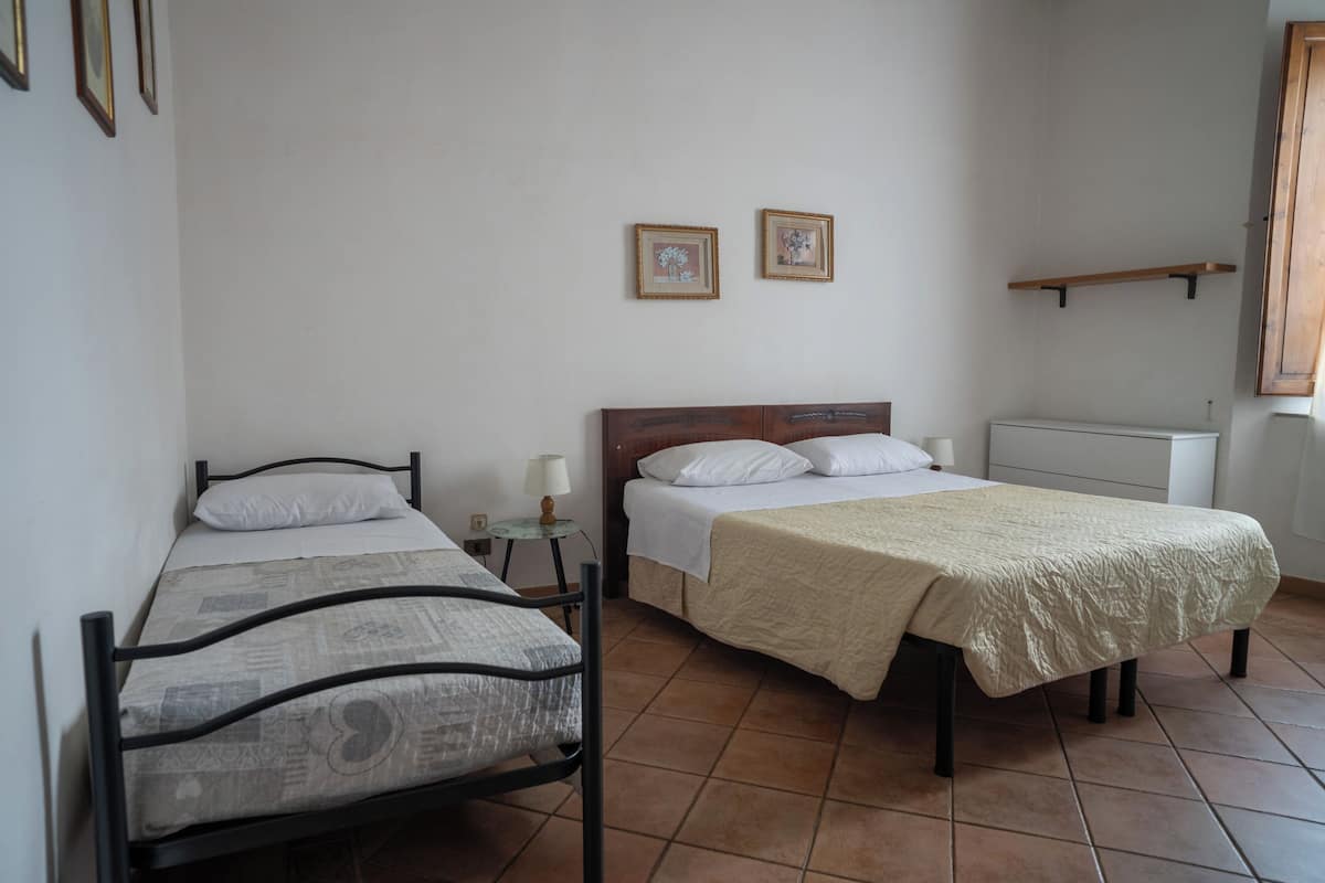 A room with two beds, a small table with a lamp, and a radiator.