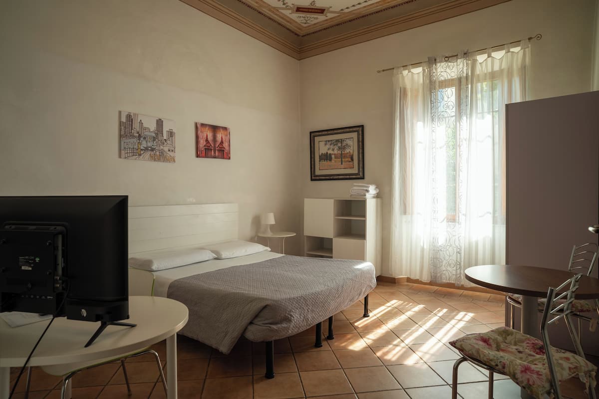 A bedroom with a bed, a desk, a chair, a TV, and artwork on the walls.