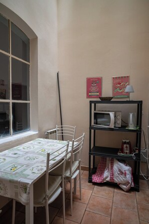 Een keuken met een tafel, stoelen, een magnetron, een waterkoker en een plank met keukengerei.