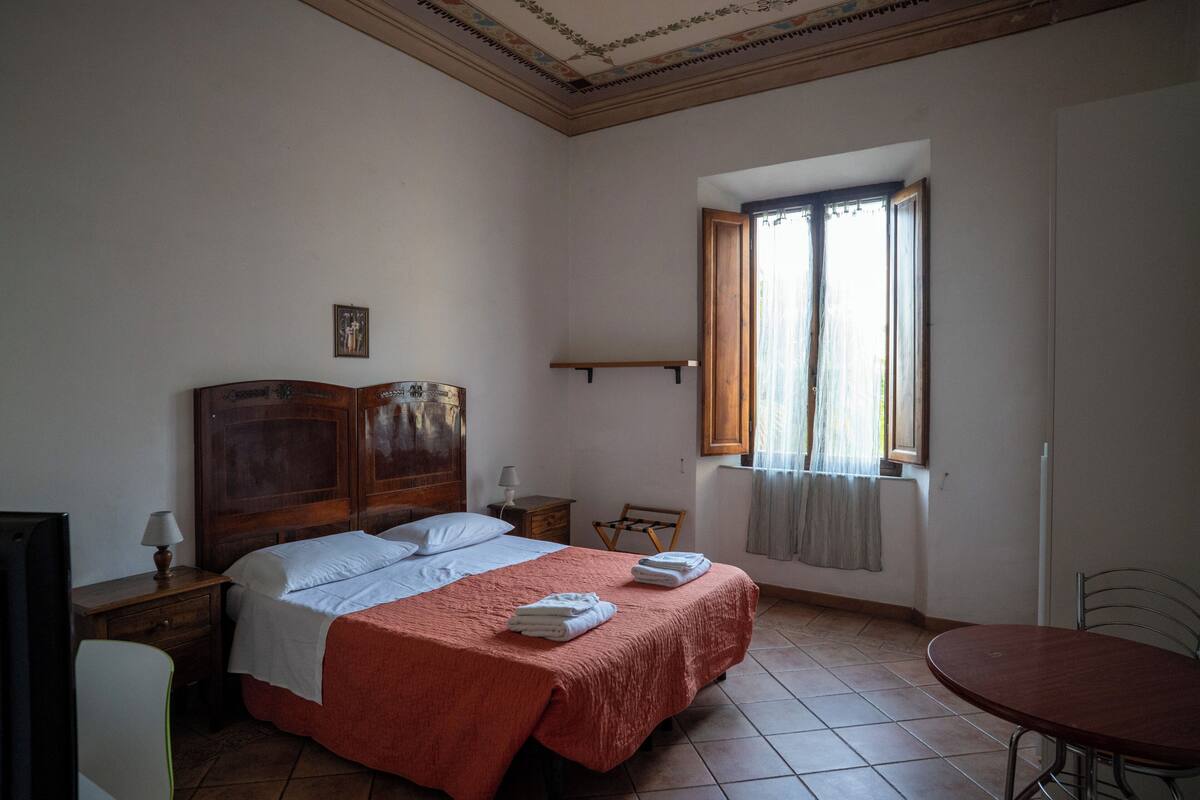 A bedroom with a bed, bedside tables, a chair, a table, and a window.