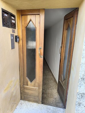 Een houten deur met een metalen handgreep, een brievenbus en een intercom bevestigd aan de muur.
