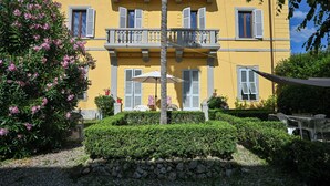 Ein gelbes Gebäude mit Balkonen, einer Steinmauer und einem Garten mit rosa Blumen.