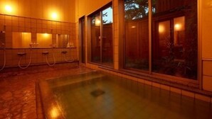 Un espace piscine extérieure chauffé, doté de murs carrelés et d’une structure en verre.