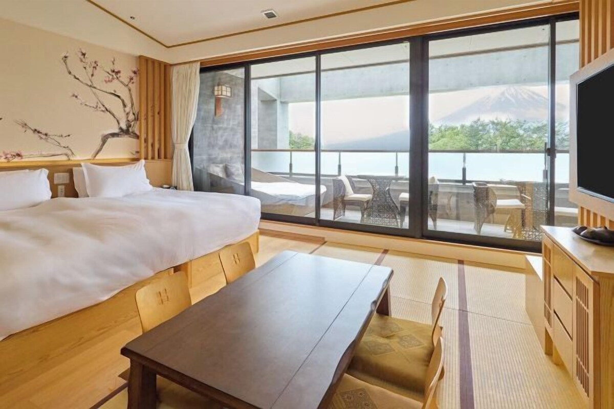 Une chambre d’hôtel avec un lit, une table à manger, une télévision et une grande fenêtre donnant sur une vue sur la montagne.