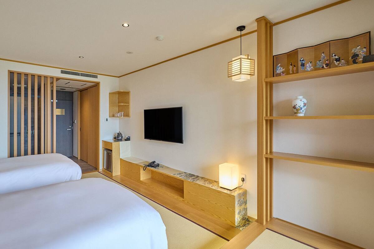A hotel room with two beds, a TV, a wooden shelf with decorative items, and a traditional Japanese sliding door.