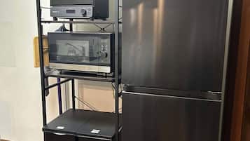 A kitchen with a stainless steel refrigerator, a microwave, and a toaster on a black metal shelf.
