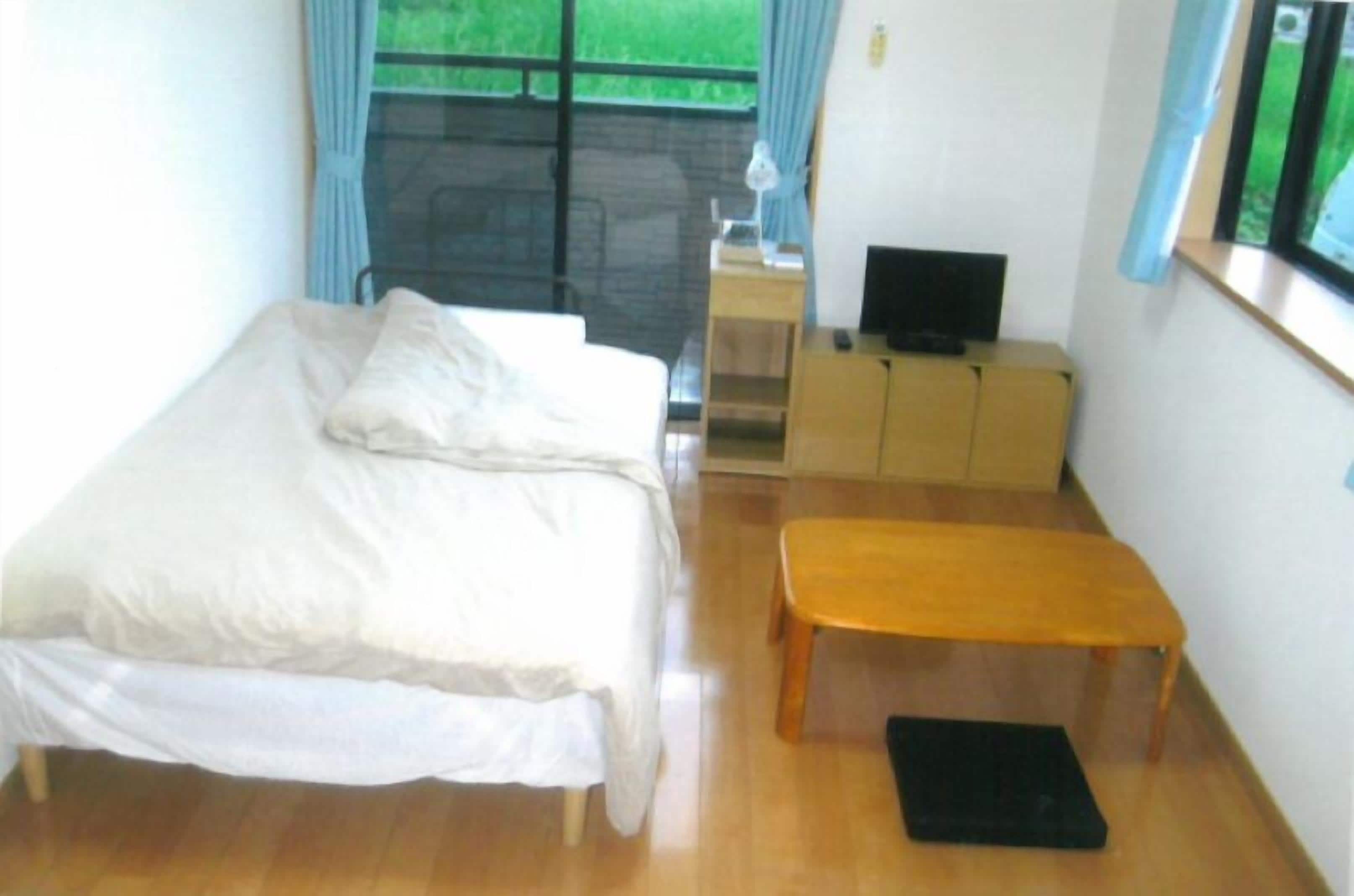 Un dormitorio con una cama, un banco, un televisor y una ventana con cortinas.