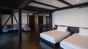 Ein modernes Hotelzimmer mit zwei Betten, einer Couch, einem Esstisch und Blick auf die Stadt.