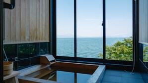 Ein modernes Badezimmer mit einem Holzschrank, einer Badewanne und einem großen Fenster mit Blick auf das Meer und die Berge.