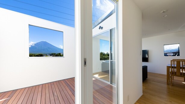 A modern interior with a wooden deck, a glass door leading to a balcony, and a television on the wall. - Frame View Mt.fuji Villa West (Fujikawaguchiko)