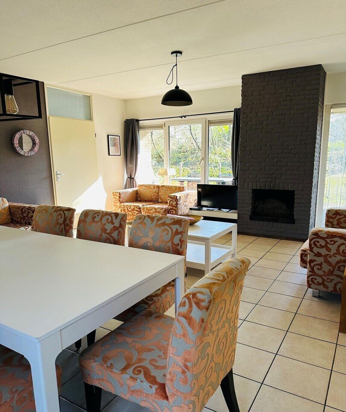 A living room with a white table, patterned sofas, a TV, and a fireplace.