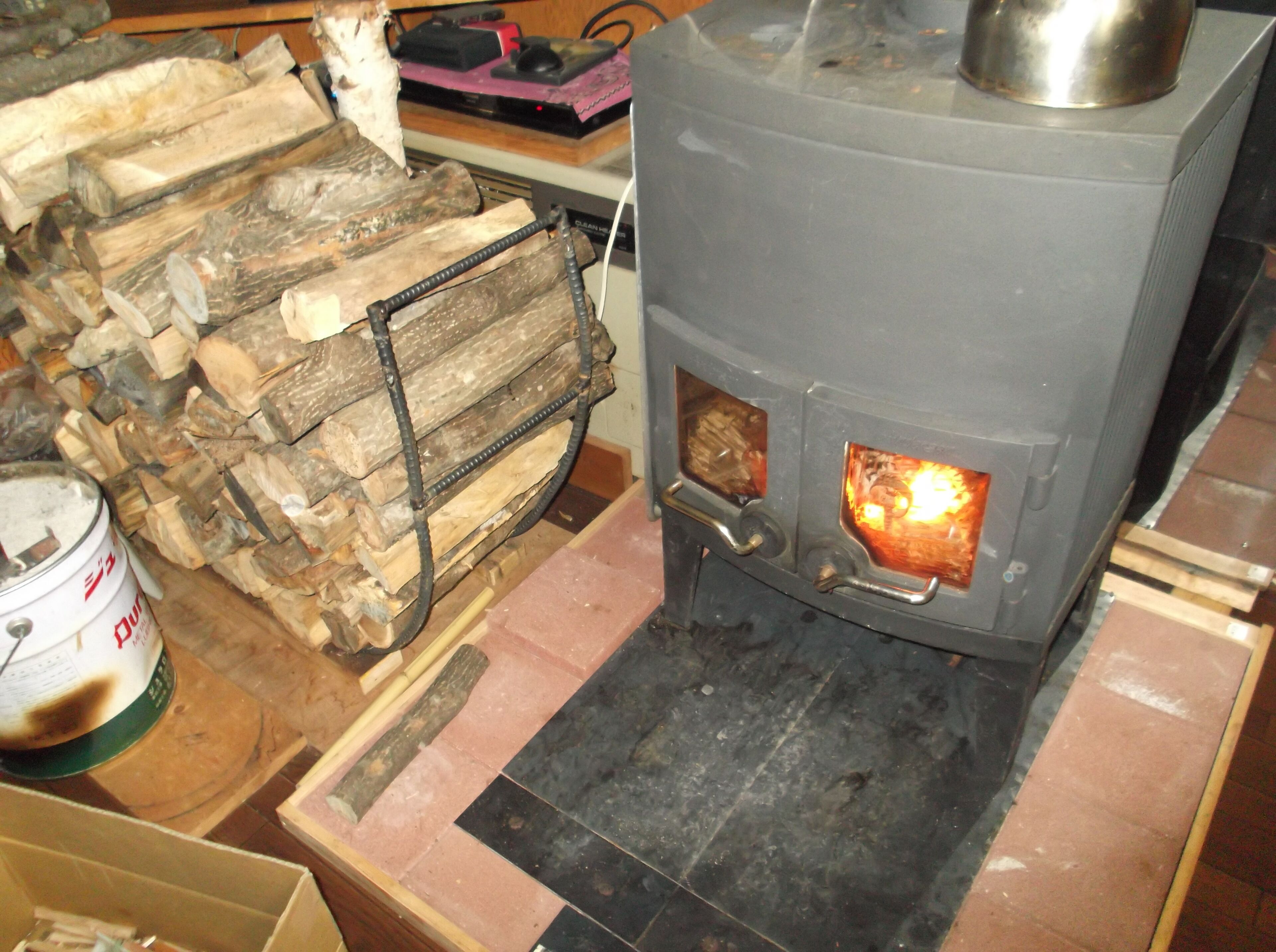A wood stove with a metal top, a fire burning inside, and a stack of firewood beside it.