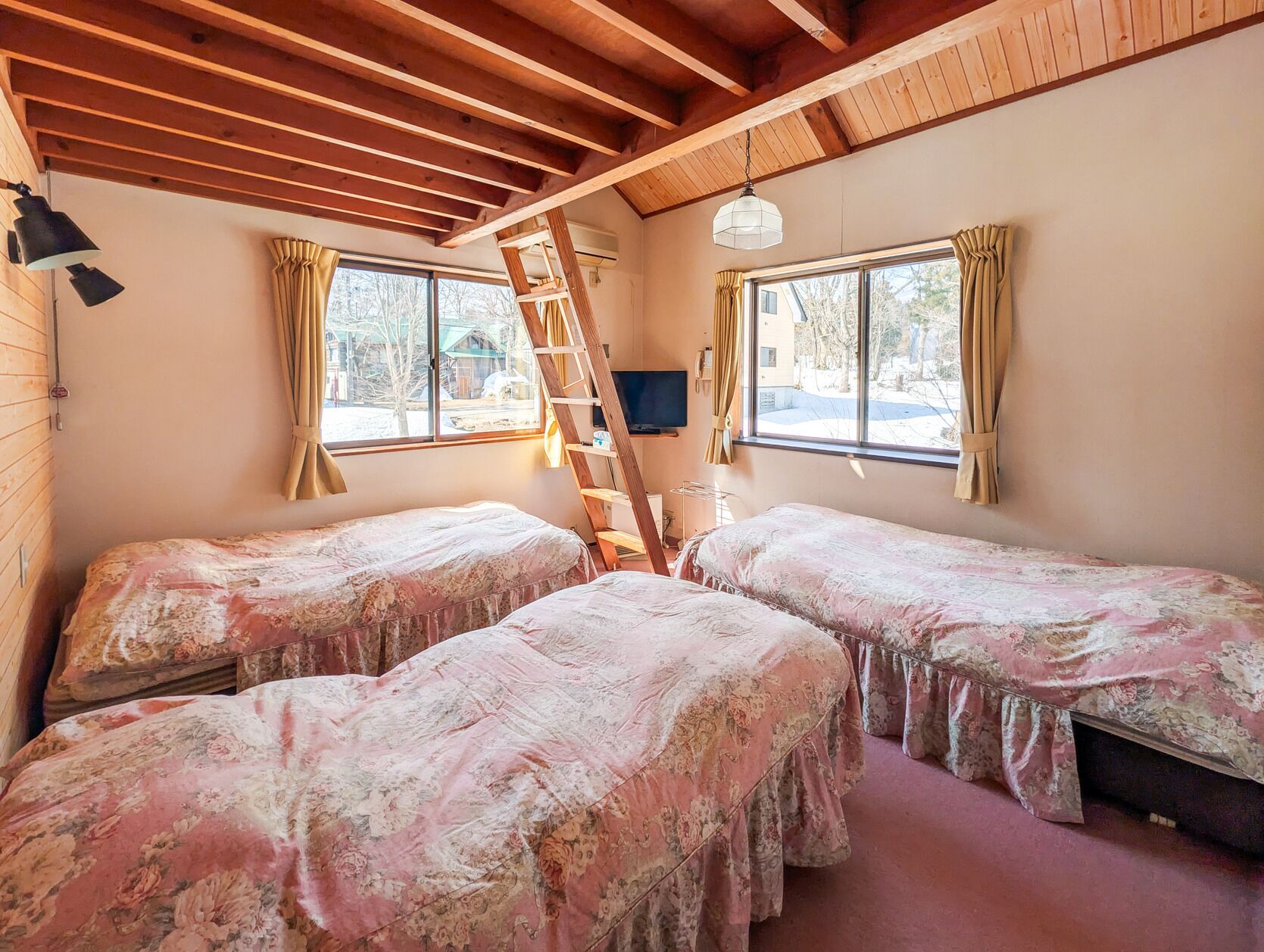 A room with two beds, a ladder, a TV, and windows with curtains.