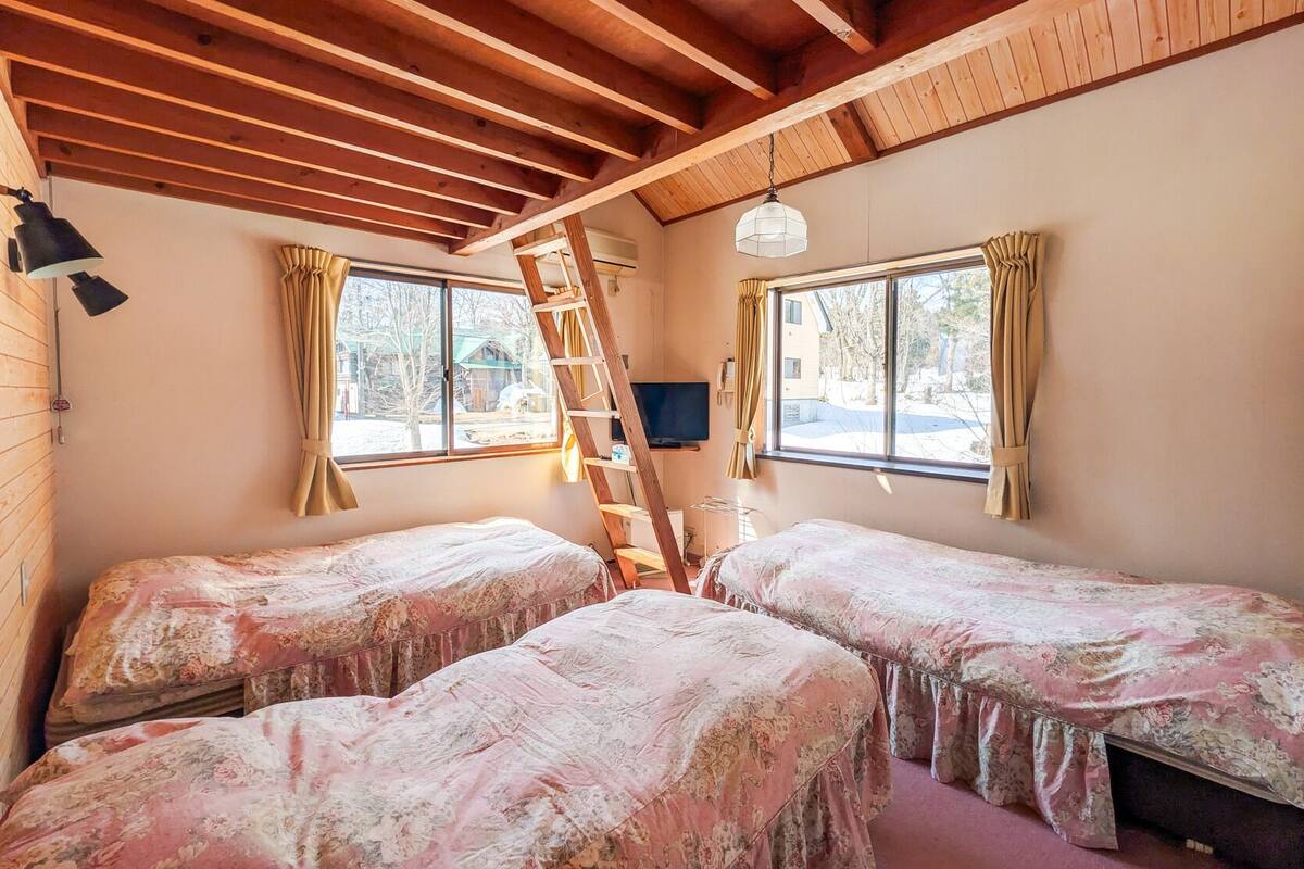 Une chambre avec deux lits, une échelle, un téléviseur et des fenêtres avec des rideaux.