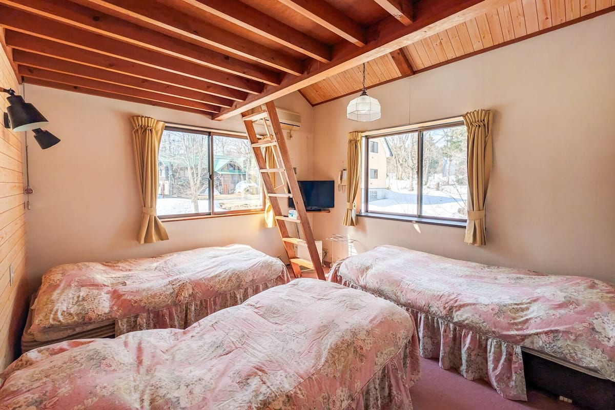 Une chambre avec deux lits, une échelle, un téléviseur et des fenêtres avec des rideaux.