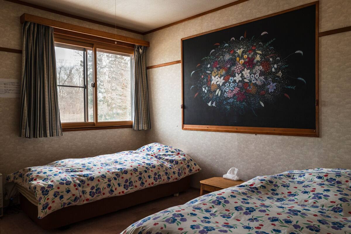 Une chambre avec deux lits, une fenêtre avec des rideaux, un tableau au mur et une petite table de chevet.