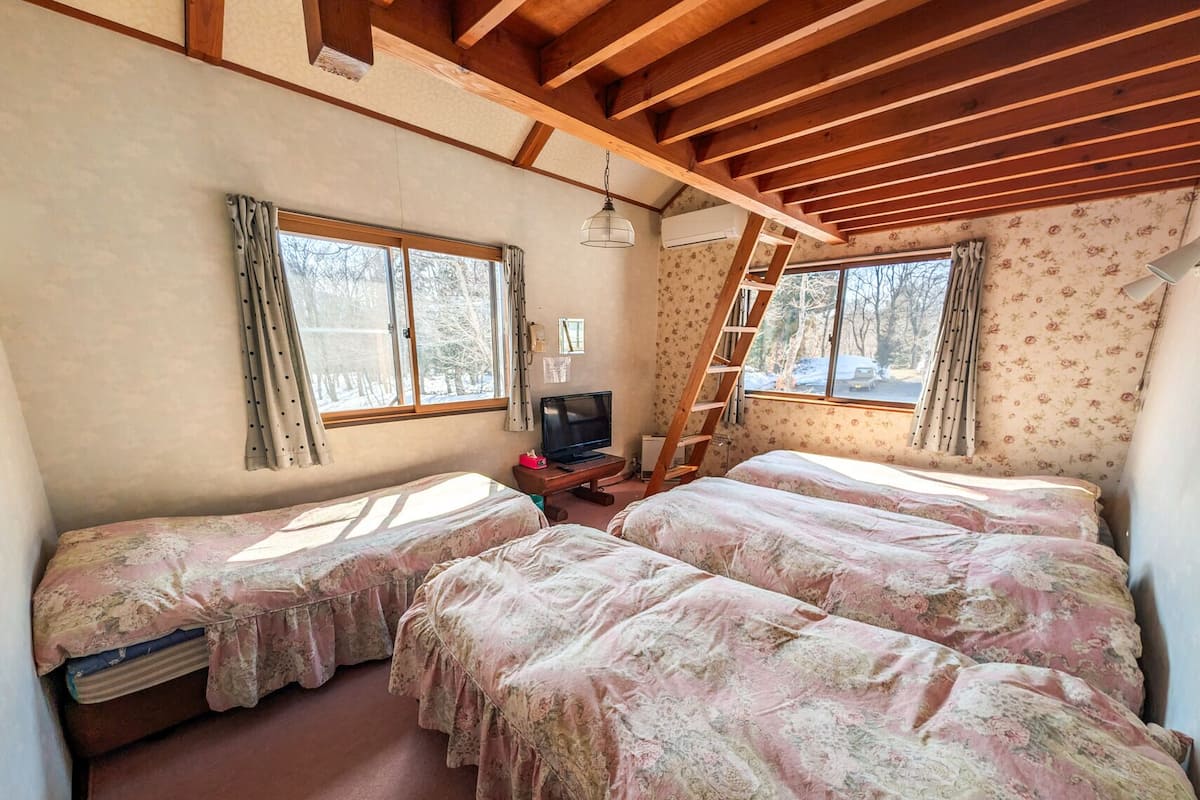 Une chambre avec deux lits, une télévision, une échelle et une fenêtre donnant sur des arbres.