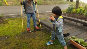 Due bambini giocano sull'altalena in un parco, con una strada e degli edifici sullo sfondo.